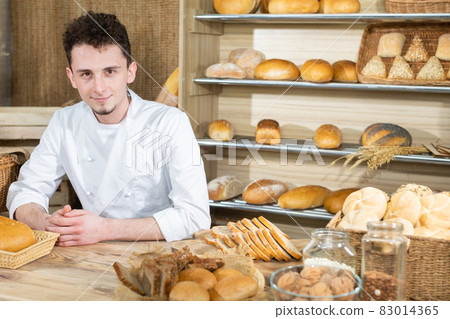 A handsome baker serves fresh bread to thirsty customers. Sale of bread in a traditional bakery store. A handsome baker serves fresh bread to thirsty customers. Sale of bread in a traditional bakery store. 83014365