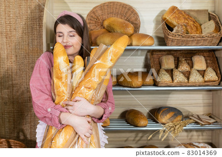 The beautiful saleswoman is delighted with the smell of fresh baguettes. Girl smelling fragrant freshly baked rolls. The beautiful saleswoman is delighted with the smell of fresh baguettes. Girl smelling fragrant freshly baked rolls. 83014369