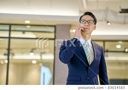 A businessman with glasses holding a smartphone 83014583