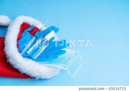 Gift set for Christmas and New Years 2021 holidays. A hygienic set of a medical mask, gloves, a disinfectant and a syringe with a vaccine and a coronavirus chip in a Santa Claus hat. Vaccination 2021 Gift set for Christmas and New Years 2021 holidays. A hygienic set of a medical mask, gloves, a disinfectant and a syringe with a vaccine and a coronavirus chip in a Santa Claus hat. Vaccination 2021 83014715