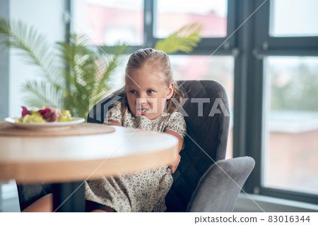 A small girl looking unpleased while looking at the food on the table A small girl looking unpleased while looking at the food on the table 83016344