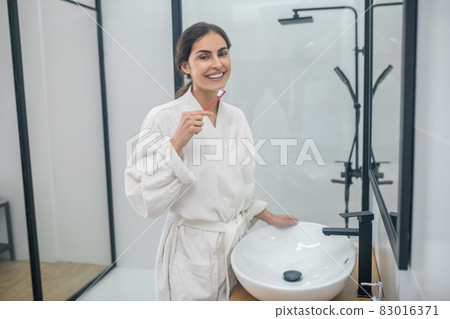 A woman in a white bath robe doing morning procedures in the bathroom A woman in a white bath robe doing morning procedures in the bathroom 83016371