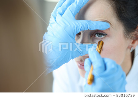 Doctor shines light into patient eye to check pupil closeup 83016759