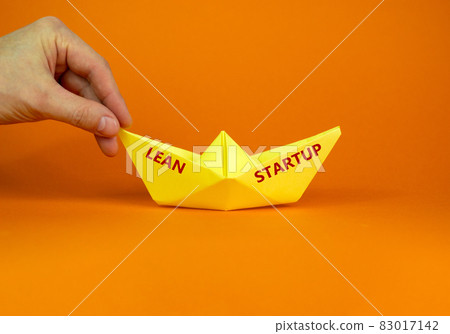 Image of businessman pushing paper made origami boat forward in a conceptual image. Text 'lean startup'. Over orange background with copy space. Business concept. Image of businessman pushing paper made origami boat forward in a conceptual image. Text 'lean startup'. Over orange background with copy space. Business concept. 83017142