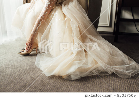Bride with lace dress puts on her wedding shoes and straightens them with her hand 83017509