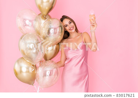 Photo of cute girl raises up glass of champagne holds many air balloons. came to party. Celebration Photo of cute girl raises up glass of champagne holds many air balloons. came to party. Celebration 83017621