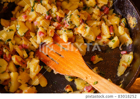 roasted domestic potatos in a frying pan with wooden spatula close-up 83018252