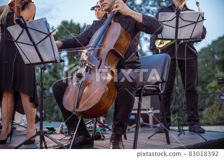 Male musician playing violoncello in orchestra on the street Male musician playing violoncello in orchestra on the street 83018392