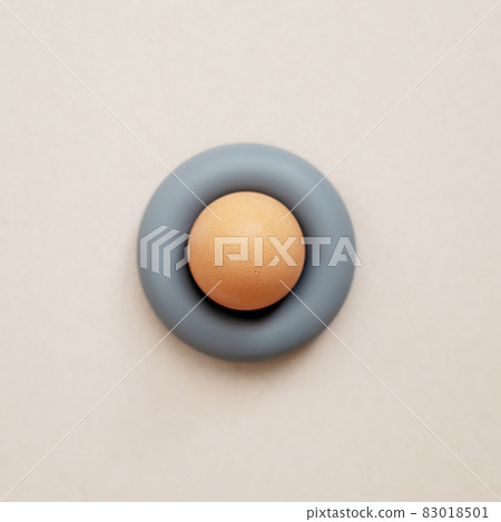 A beige egg stands in a gray rubber expander on a light background. Top view A beige egg stands in a gray rubber expander on a light background. Top view 83018501