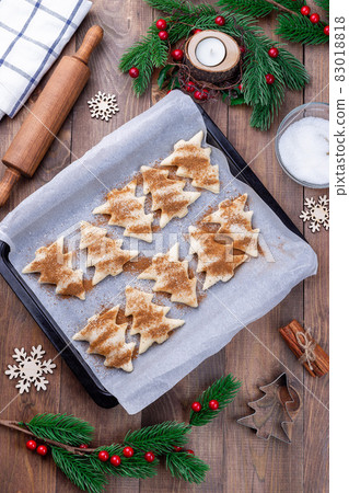 Making Christmas tree shaped puff pastry cookies with sugar and cinnamon, ready to bake cookie on parchment Making Christmas tree shaped puff pastry cookies with sugar and cinnamon, ready to bake cookie on parchment 83018818
