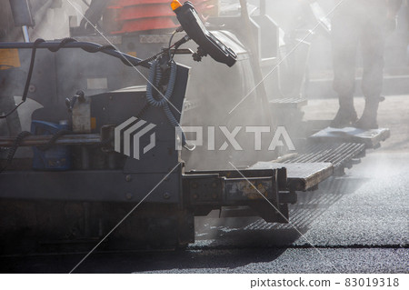 close-up view of asphalting paver machine during road street repairing works at day light with smoke and steam in the air 83019318