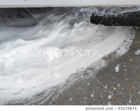 Soap sud waste flows to floor drain grid in car washing garage. Full frame close-up with selective focus. 83019674