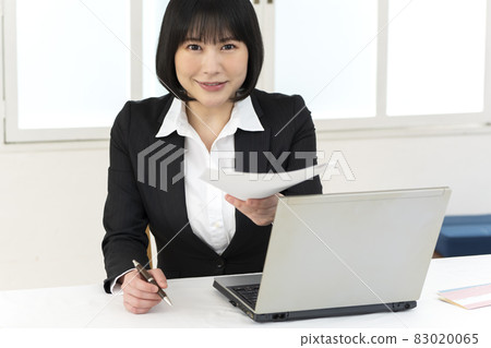 Young woman sitting at a desk and handing over documents 83020065