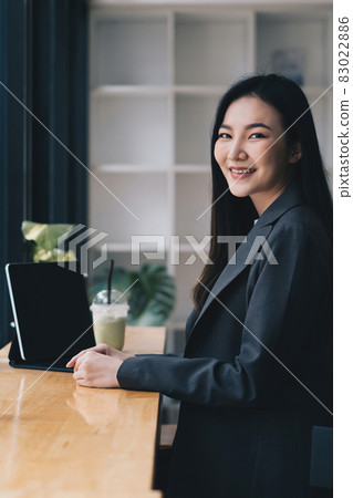 Portrait of beautiful fund managers sitting on chair with tablet on wooden desk in cafe shop. Portrait of beautiful fund managers sitting on chair with tablet on wooden desk in cafe shop. 83022886