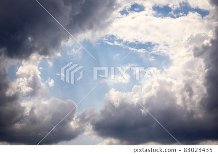 Blue open sky with dark and white clouds and light beams Blue open sky with dark and white clouds and light beams 83023435