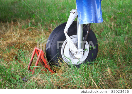 Black plane wheel resting on red blocker standing on green grass Black plane wheel resting on red blocker standing on green grass 83023436