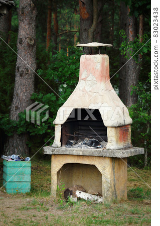 Old clay furnace with logs standing outdoors near the forest and full garbage bin Old clay furnace with logs standing outdoors near the forest and full garbage bin 83023438