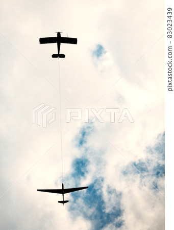 Two planes flying high in the sky with heavy clouds one pulling another Two planes flying high in the sky with heavy clouds one pulling another 83023439
