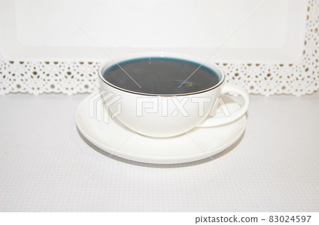 The mood color is blue - blue tea in a white mug, which stands on a white saucer and a white tray. The mood color is blue - blue tea in a white mug, which stands on a white saucer and a white tray. 83024597