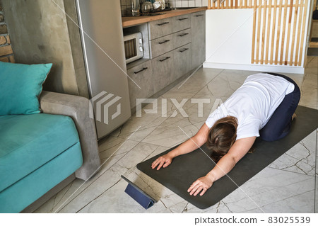 Young woman going yoga exercise at kitchen. Health care online lessons. Fitness Young woman going yoga exercise at kitchen. Health care online lessons. Fitness 83025539