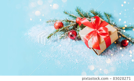 Festive box with a red bow on a blue background with Christmas toys balls branch of fluffy spruce sparkles and confetti . New Year Christmas concept. Flat festive mockup with copy space Festive box with a red bow on a blue background with Christmas toys balls branch of fluffy spruce sparkles and confetti . New Year Christmas concept. Flat festive mockup with copy space 83028271
