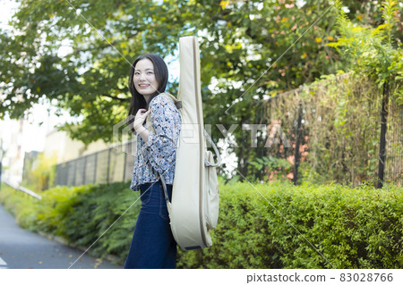 A woman walking with a guitar case 83028766