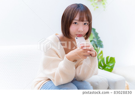 A woman holding a smartphone and looking at me with a smile 83028830