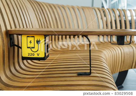 A socket with a device charging sign on a wooden bench at the airport. 83029508