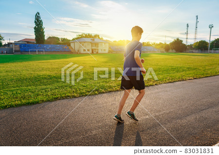 teen boy running along the stadium track, a soccer field with green grass - concept of sports and health teen boy running along the stadium track, a soccer field with green grass - concept of sports and health 83031831