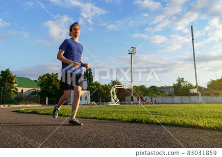 concept of sports and health - teen boy runs along the stadium track, a soccer field with green grass. 83031859