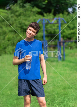 teenage boy exercising outdoors, sports ground in the yard, he opens a bottle of water and drinks, healthy lifestyle teenage boy exercising outdoors, sports ground in the yard, he opens a bottle of water and drinks, healthy lifestyle 83031921