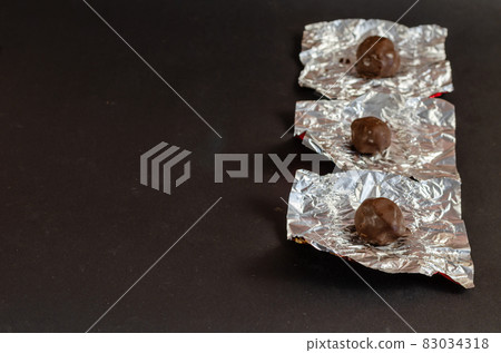 Round chocolates in unwrapped silver wrapper on a black backgrou Round chocolates in unwrapped silver wrapper on a black backgrou 83034318