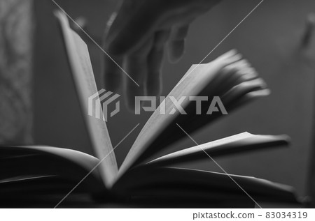 A defocused shot of an old open book and a man's hand. Dusty pag 83034319