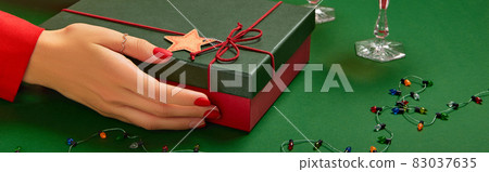 Womans hands with trendy red manicure holding gift box on green background 83037635