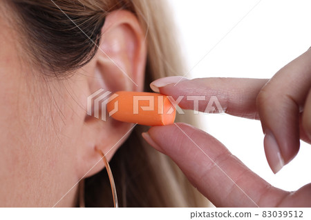 Woman inserts orange earplugs into ears closeup Woman inserts orange earplugs into ears closeup 83039512