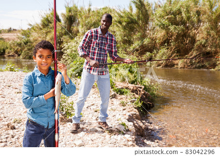Man and boy holding fish on rod Man and boy holding fish on rod 83042296