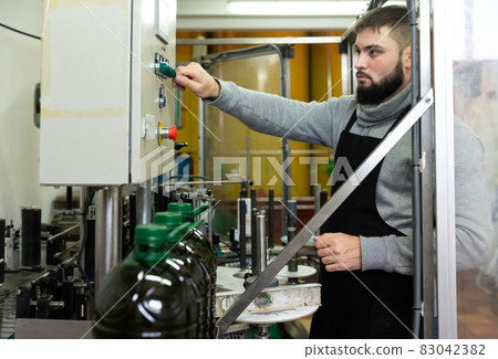 Guy pouring olive oil in plastic bottles Guy pouring olive oil in plastic bottles 83042382
