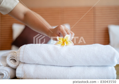 A hotel maid stacked towels on the bed and placed flowers on the towels in a hotel room A hotel maid stacked towels on the bed and placed flowers on the towels in a hotel room 83043550