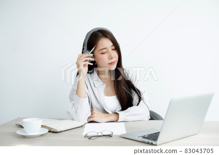 Video call, a young Asian woman wearing headphones, communicates via online video long distance, looking at the digital laptop screen, happily greeted with a friend Video call, a young Asian woman wearing headphones, communicates via online video long distance, looking at the digital laptop screen, happily greeted with a friend 83043705