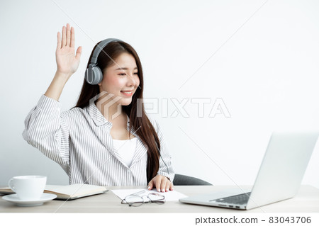 Video call, a young Asian woman wearing headphones, communicates via online video long distance, looking at the digital laptop screen, happily greeted with a friend Video call, a young Asian woman wearing headphones, communicates via online video long distance, looking at the digital laptop screen, happily greeted with a friend 83043706