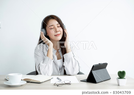 Video Calling a young Asian woman wearing headphones communicates via online long-distance video on a digital tablet happily greetings with a friend 83043709