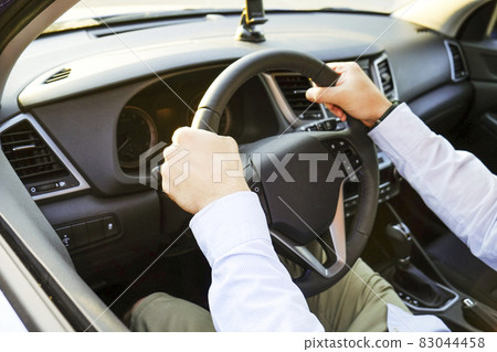 Car interior with male driver sitting behind the wheel, soft sunset light. Luxurious vehicle dashboard and electronics. 83044458
