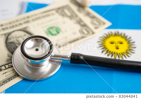 Black stethoscope on Argentina flag background with US dollar banknotes, Business and finance concept. Black stethoscope on Argentina flag background with US dollar banknotes, Business and finance concept. 83044841