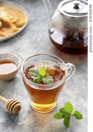 Glass cup with herbal tea with teapot and mint leaves. Morning tea. Glass cup with herbal tea with teapot and mint leaves. Morning tea. 83046696