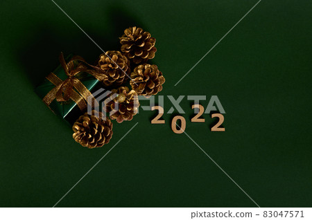 Flat lay. Gold pine cones, luxury present in glitter green wrapping gift paper with golden bow and wooden numerals 2022 isolated on dark green background with copy space for New Year and Christmas ad Flat lay. Gold pine cones, luxury present in glitter green wrapping gift paper with golden bow and wooden numerals 2022 isolated on dark green background with copy space for New Year and Christmas ad 83047571