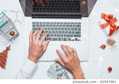 Online gift. Gift box red ribbon for Christmas, trolley and laptop in flat lay internet online shopping composition. Xmas sales and discounts promotions. 83047861