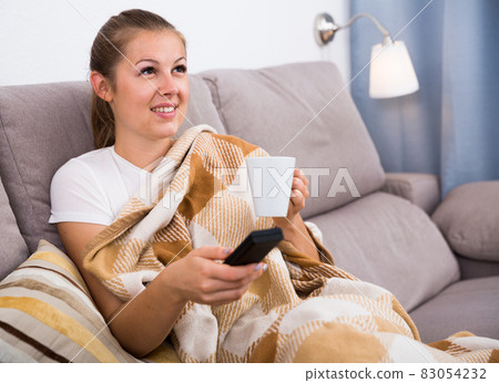 Young female is watching TV and sitting with tea Young female is watching TV and sitting with tea 83054232