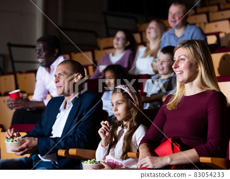 Cheerful family watching a movie and eating popcorn in cinema Cheerful family watching a movie and eating popcorn in cinema 83054233