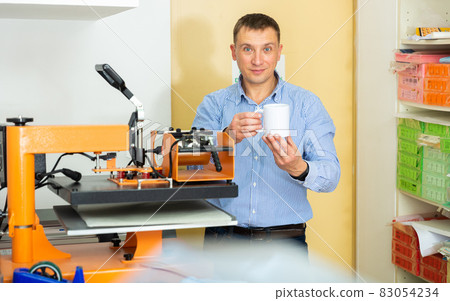 Man uses machine to print on ceramic mug Man uses machine to print on ceramic mug 83054234