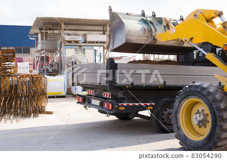 Excavator moving sand to empty truck at hardware store 83054290